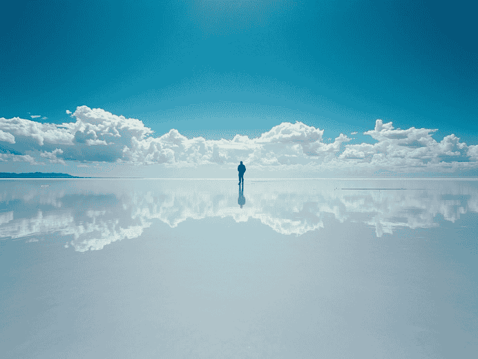 Un viaggiatore solitario cammina sul deserto di sale Salar de Uyuni riflesso come uno specchio.
