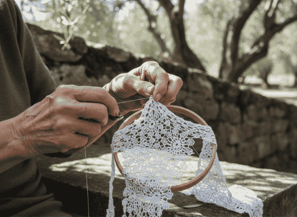 Mani anziane e sapienti al lavoro per creare un merletto a punto d'Irlanda, tradizione di Isola Maggiore.